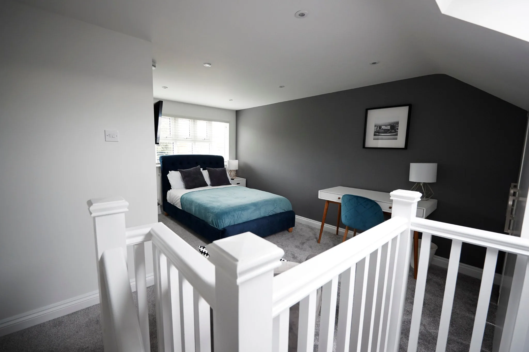 Finished loft bedroom with a blue bed, desk, sloping roof and white stair balustrade