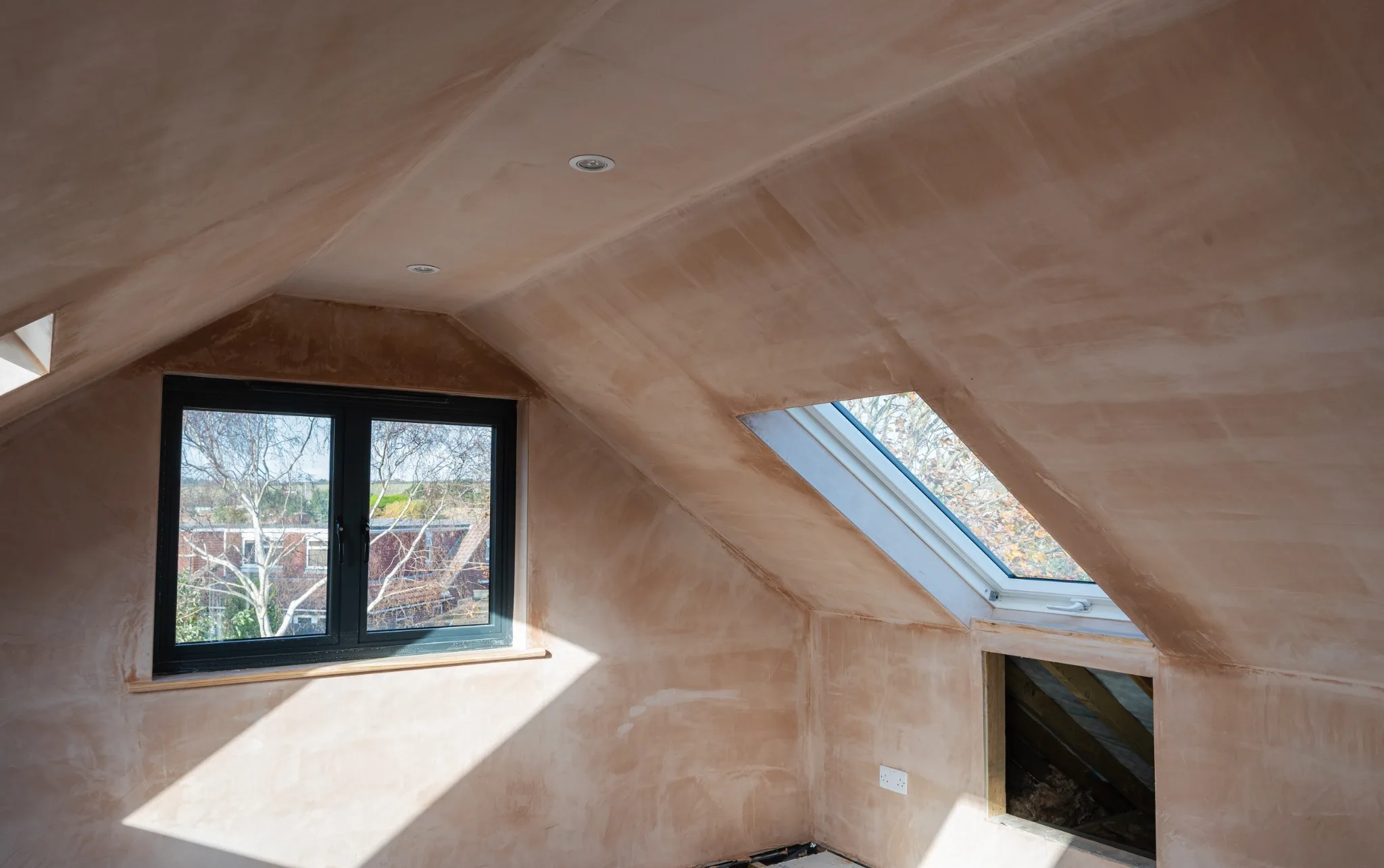 Plastered loft interior with a rooflight and black-framed window during the finishing stage
